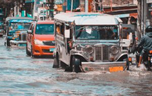 A passenger jeepney on the Malabon–Letre–Monumento route wades through knee-deep floodwater, followed by cars and a motorcycle rider